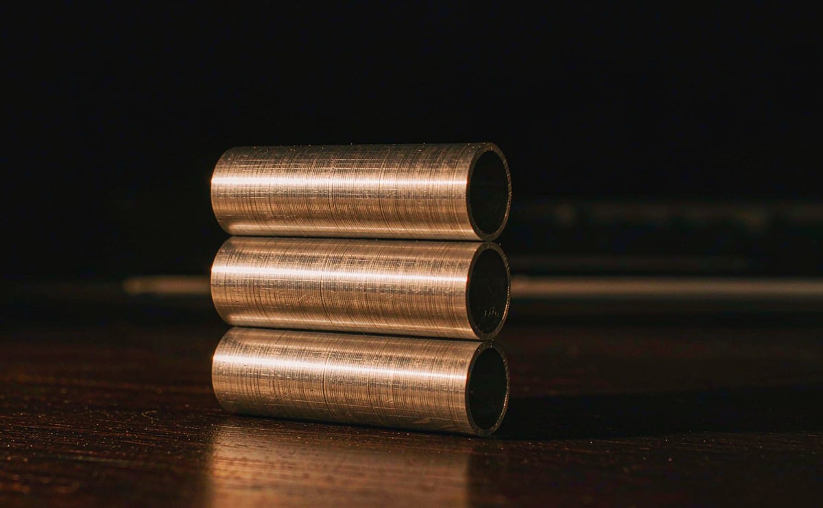 Three polished metal tubes held together side by side on a desk with no visible fastener