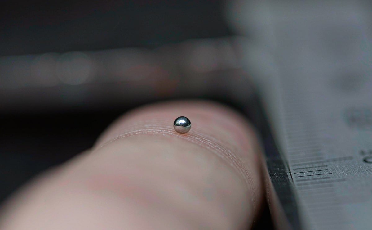 A pen ball resting on a fingertip beside precision calipers