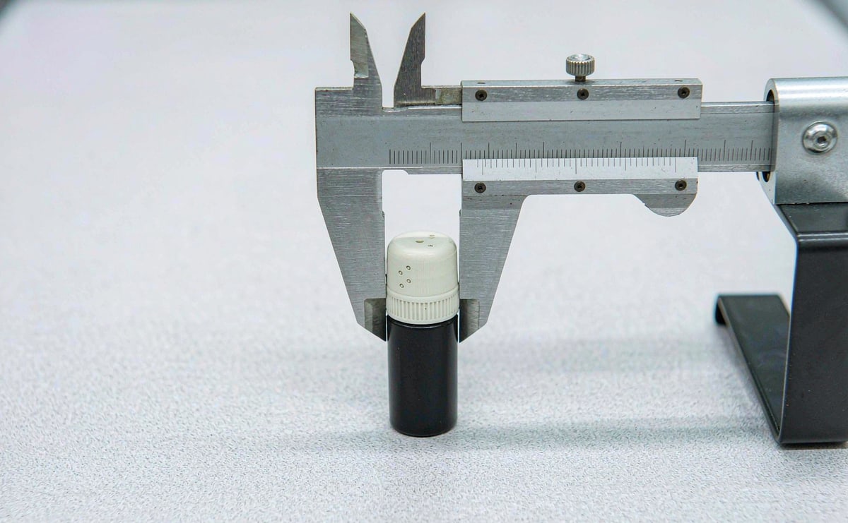 Vernier calipers measuring a single metal refill on an inspection bench