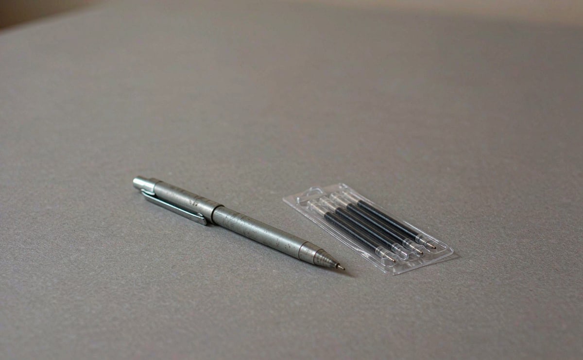 A metal pen beside a pack of standard refills on a desk
